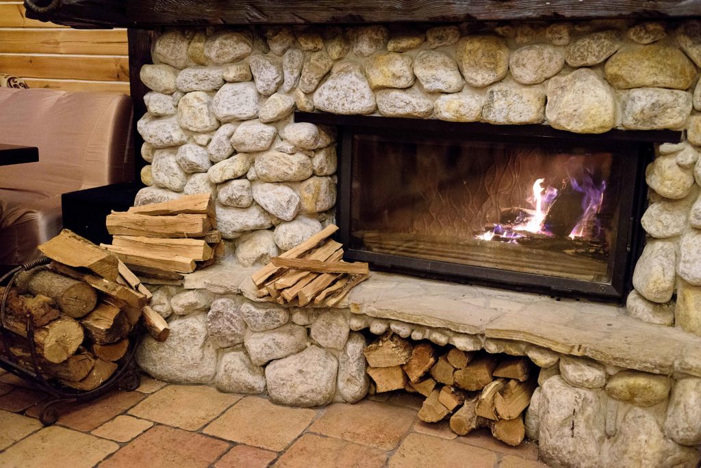 Stone fireplace with burning fire in country cottage. Flames of fire burning. Firewood against fireplace