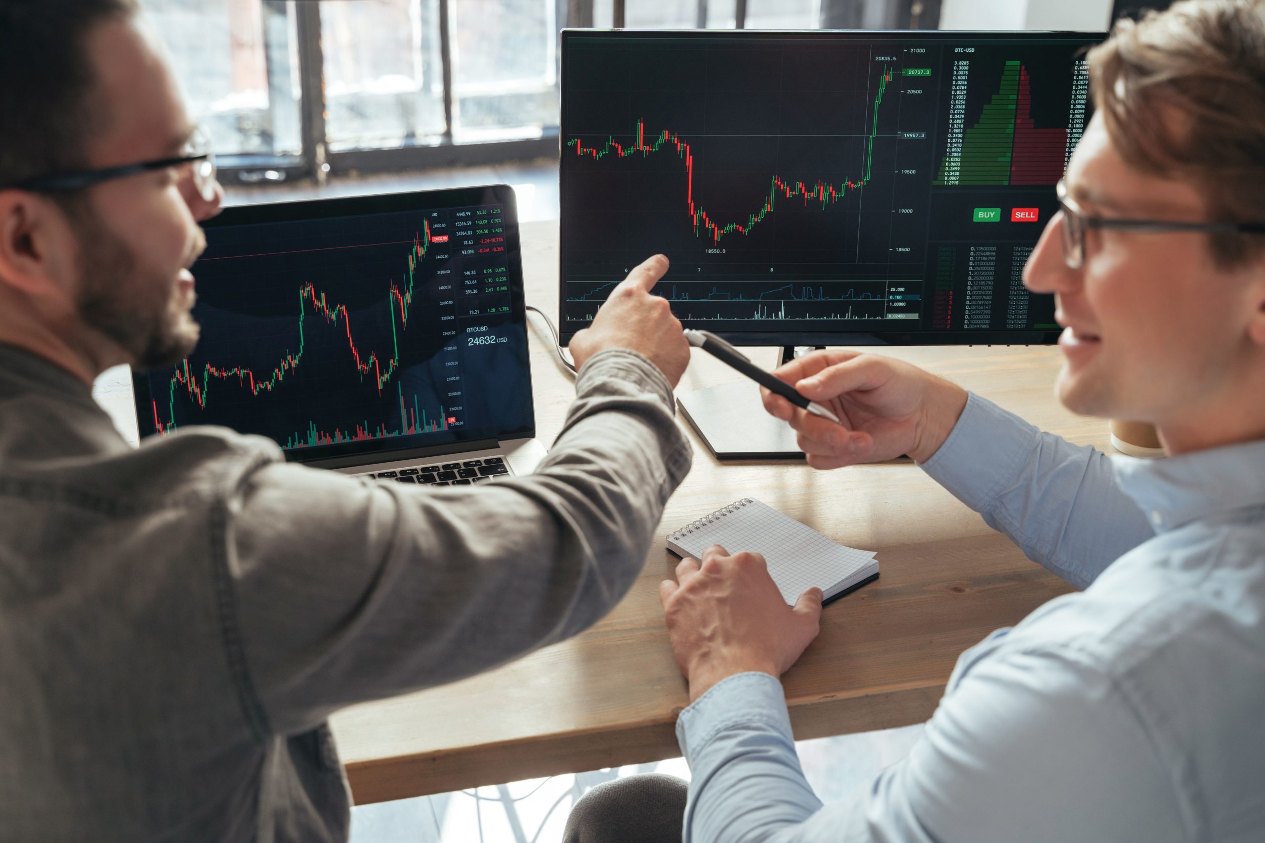 Closeup of two men trader investors sitting at office table together in front of pc, analyzing price flow, discussing rate, actions, monitoring stocks data charts. Selective focus on computer screen